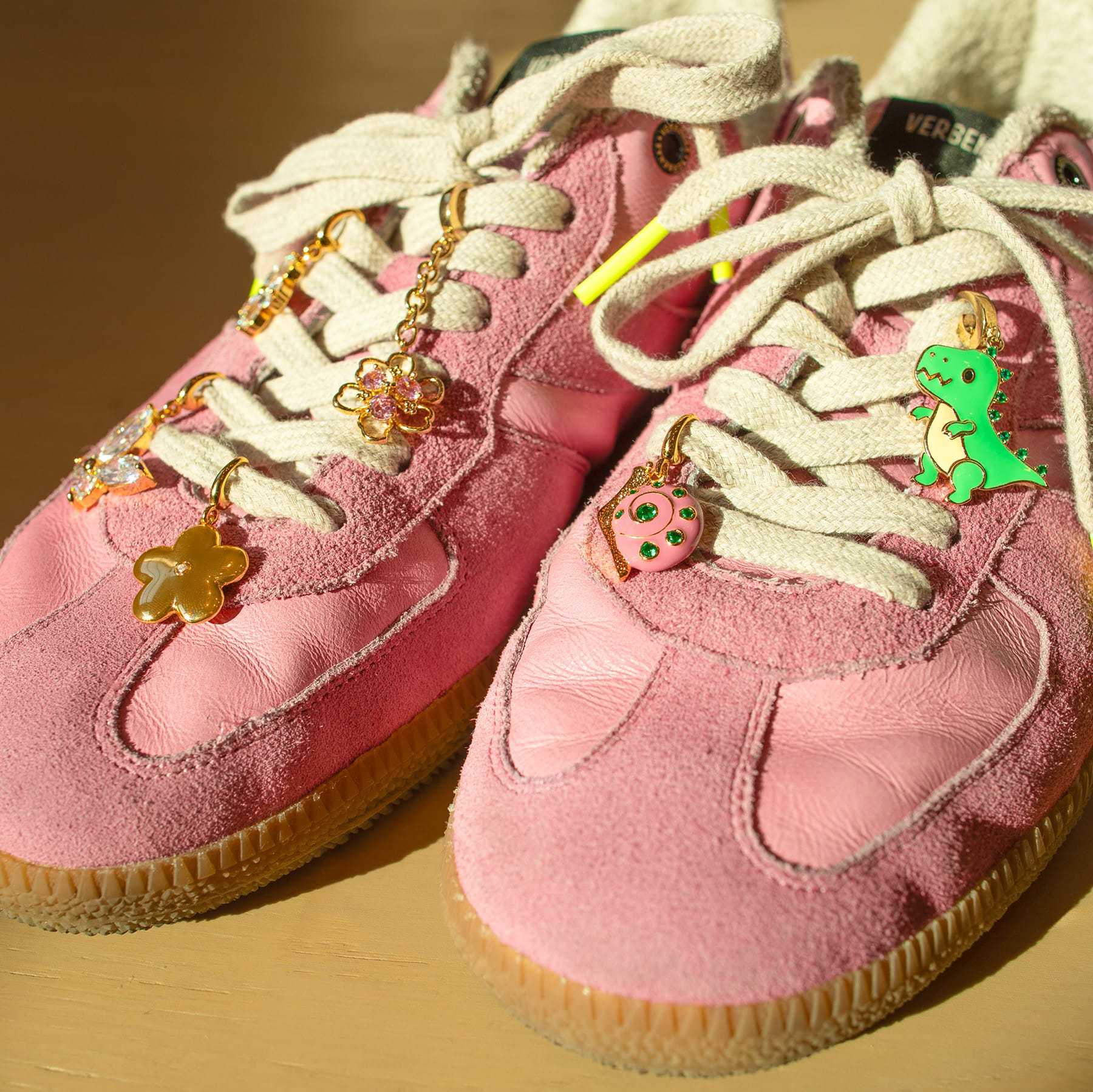 Pink sneakers decorated with stainless steel lace charms in dinosaur, donut, flower, butterfly, and star shapes